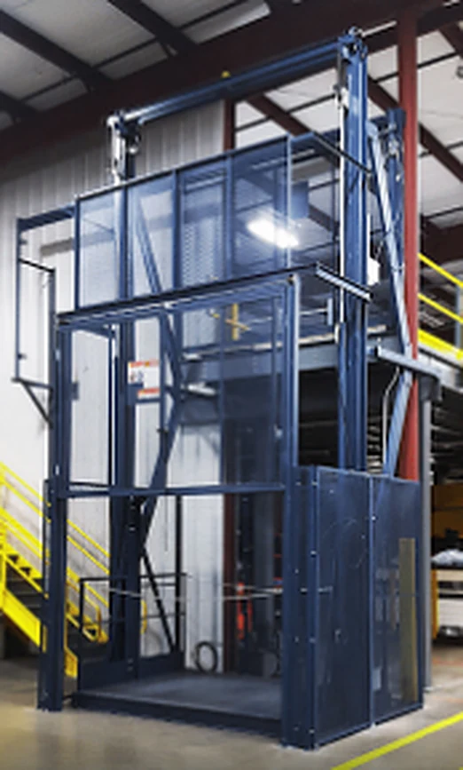 Elevador de carga industrial azul con cabina de malla instalado en una nave