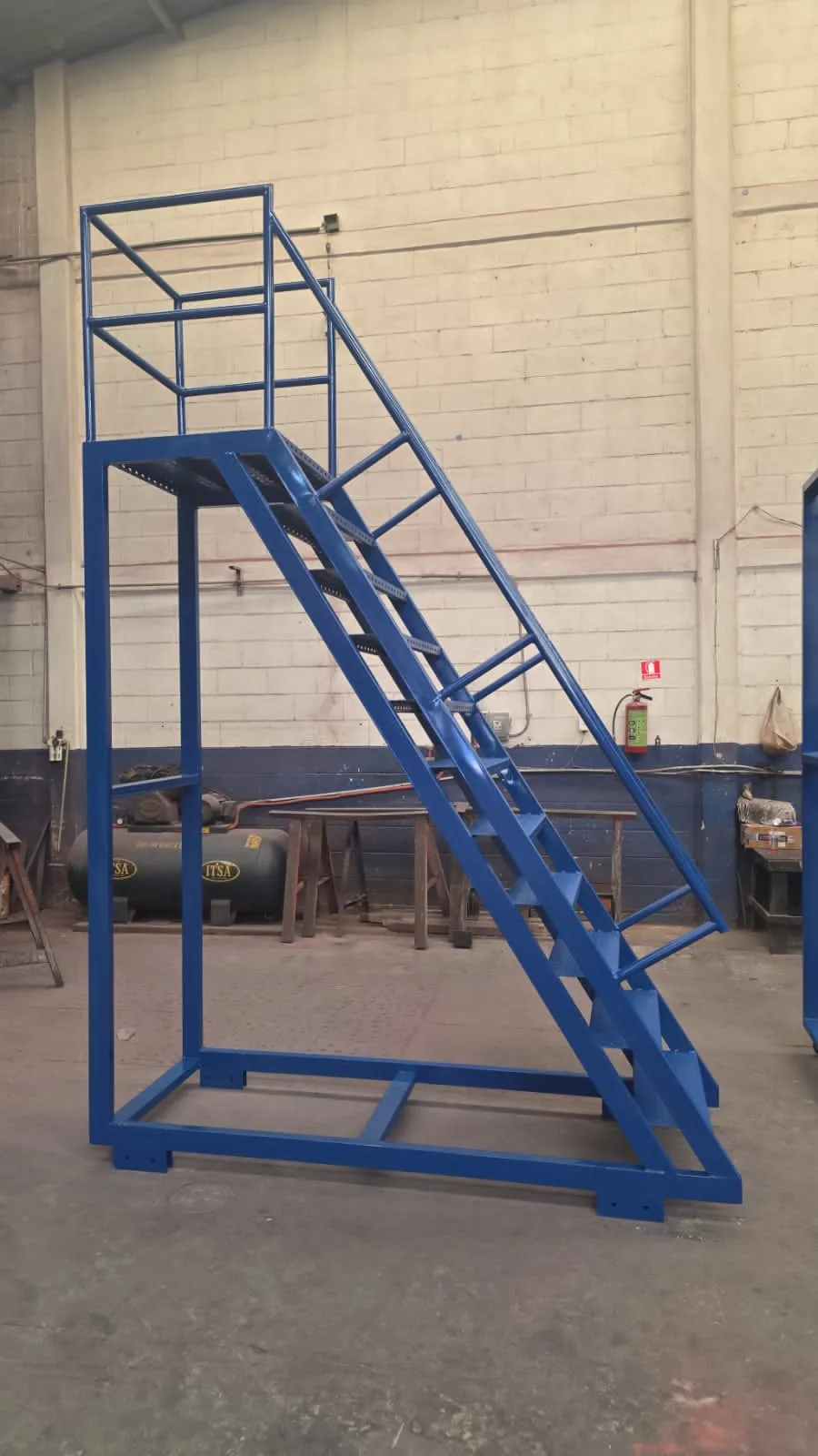Escalera industrial azul a la medida con plataforma, fabricada por Montrack